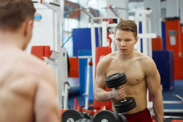 Jeune homme athlétique soulevant des haltères dans la salle de gym . — Photo