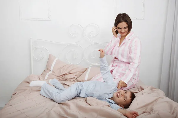 Jonge, mooie vrouw en zoon in roze en blauwe pyjama in bed met — Stockfoto