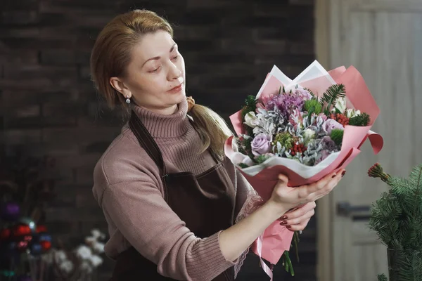 Female florist in a brown apron shows a buyer a beautiful bouque — Stock Photo, Image