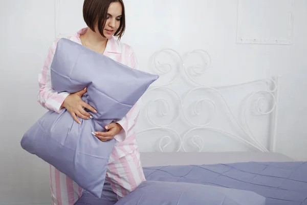 Jeune femme brune mignonne en pyjama rose fait le lit avec — Photo