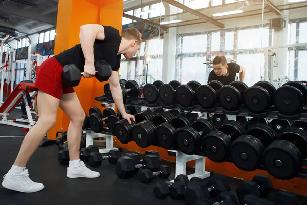 Genç, atletik adam spor salonunda dambıl kaldırma.