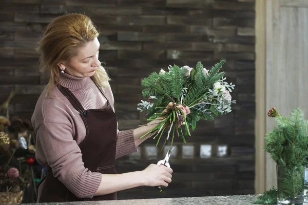 Pretty middle-aged florist woman in an apron collects a bouquet. — Stock Photo, Image