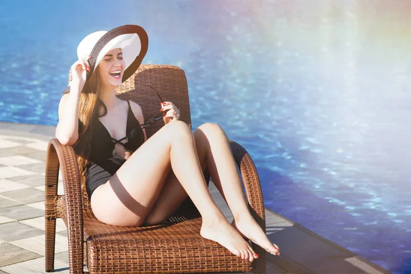 Siyah mayo ve plaj şapka genç kadın bir güverte oturur