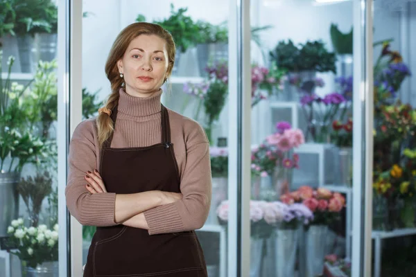 Florist woman in brown apron at flower salon in front of fridge