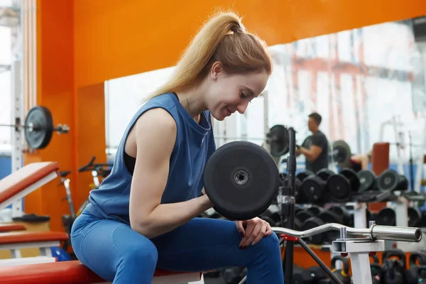 Joven, bonita chica con el pelo largo levantando pesas en el gimnasio . —  Fotos de Stock