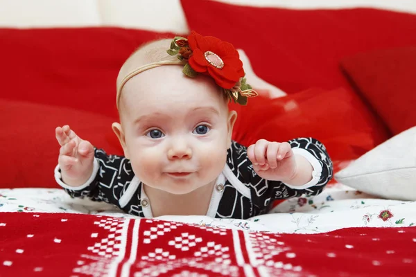 Baş elbisesini kırmızı bir arka plan üzerinde bir çiçek güzel beş aylık bebek kız. Bebeğim bak. Anne bakım. Çocuk Bakımı. Yakın çekim.