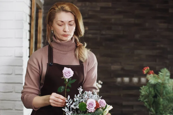 Pretty middle-aged florist woman in an apron collects a bouquet. — Stock Photo, Image