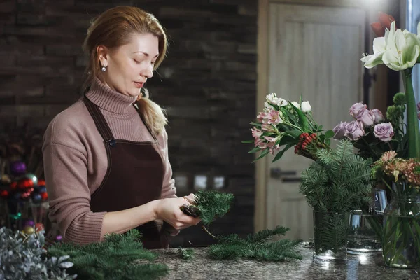 Pretty middle-aged florist woman in an apron collects a bouquet. — Stock Photo, Image