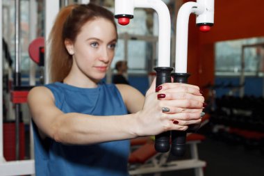 Genç ve güzel bir kadın spor salonundaki simülatörde fiziksel egzersiz yapıyor..