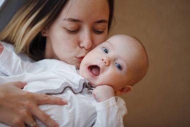 Genç mutlu anne, bebeğini kollarında pencereye doğru öpüyor. Annelik bakımı. Çocuk bakımı. Yakın plan..
