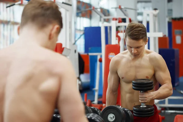 Jeune homme athlétique soulevant des haltères dans la salle de gym . — Photo