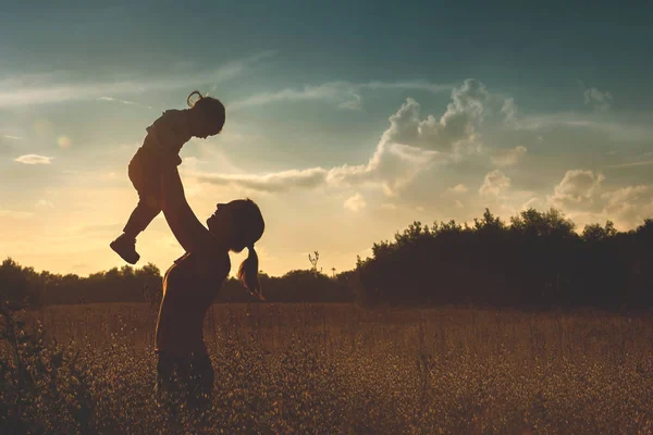 Silhueta de uma jovem mãe e sua filhinha ao pôr do sol — Fotografia de Stock