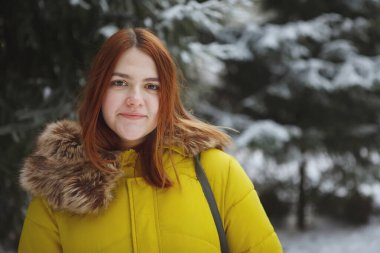 Genç, sevimli, neşeli kızıl saçlı bir kadın karlı bir ormanda.