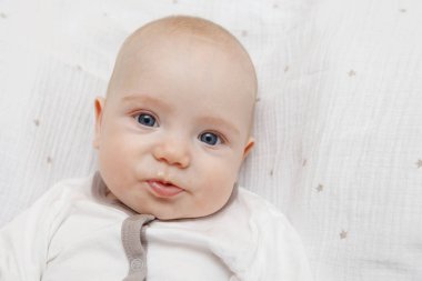 Sırtı, farklı duygular ve yüzünde bir gülümseme güzel beş aylık mavi gözlü Bebek Tulum içinde yatıyor. Bebek bak. Anne bakım. Çocuk Bakımı. Yakın çekim.