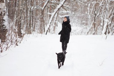 Kara labrador köpeği olan genç bir çocuk kış ormanında.
