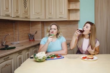 İnce kız cupcake, şişman kızın adını kıskanç yiyor. Diyet, doğru beslenme, sağlıklı yaşam tarzı.