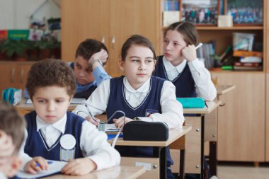 Okul çocukları okul sırasında sınıflarında masalarında otururlar.