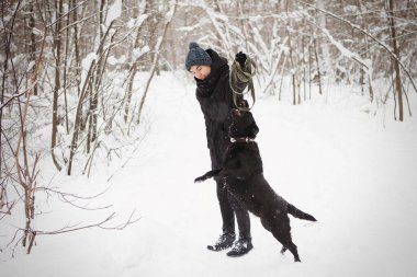 Genç çocuk kara labrador av köpeğiyle kış ormanında eğleniyor..