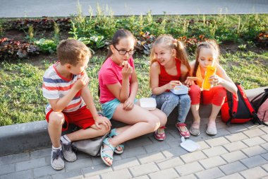 Gençler şehir parkında kaldırımda oturuyorlar..