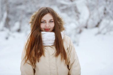 Young, pretty woman in a white knitted scarf in a snowy forest.
