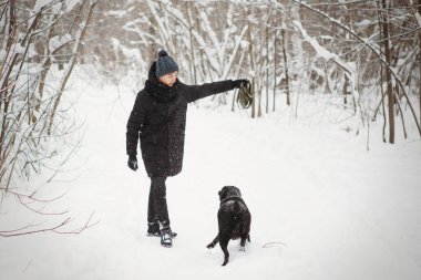 Genç çocuk kara labrador av köpeğiyle kış ormanında eğleniyor..