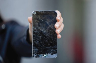 Kırık cam ekran akıllı telefon, üzgün bir kızın elinde.