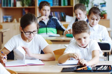 Okul çocukları okul sırasında sınıflarında masalarında otururlar.