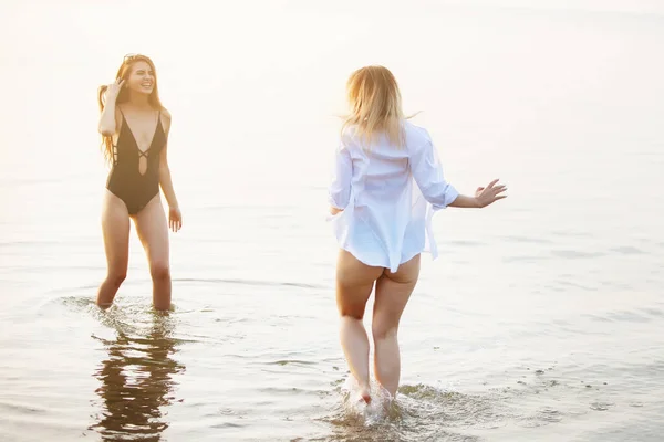 Dwie dziewczyny bawią się w morzu o zachodzie słońca. — Zdjęcie stockowe