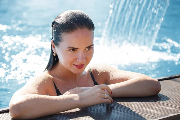 Молодая красивая женщина под водопадом в бассейне с чистым блю — стоковое фото