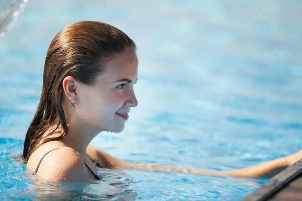 Joven hermosa mujer bajo una cascada en una piscina con blu claro — Foto de Stock