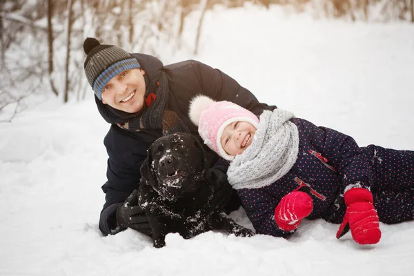 Mężczyzna i dziewczyna zabawa z jego czarny labrador retriever w zimie dla — Zdjęcie stockowe