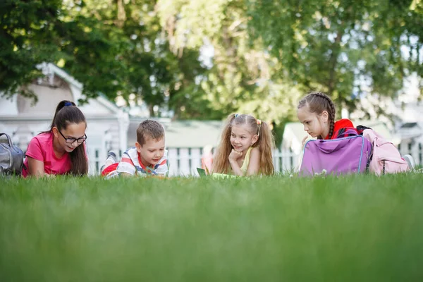 Cuatro niños sentados en la hierba verde . — Foto de Stock