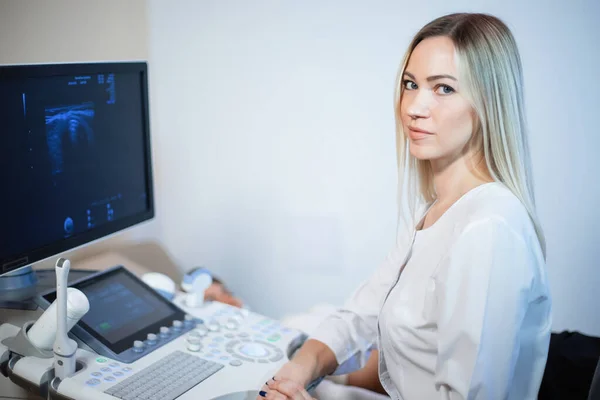 Ξανθιά γυναίκα γιατρός κοντά σε ένα υπερηχογράφημα οθόνη κοιτάζει ου — Φωτογραφία Αρχείου