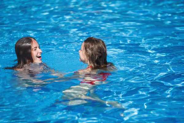 Dos mujeres guapas jóvenes nadan en la piscina con azul claro — Foto de Stock