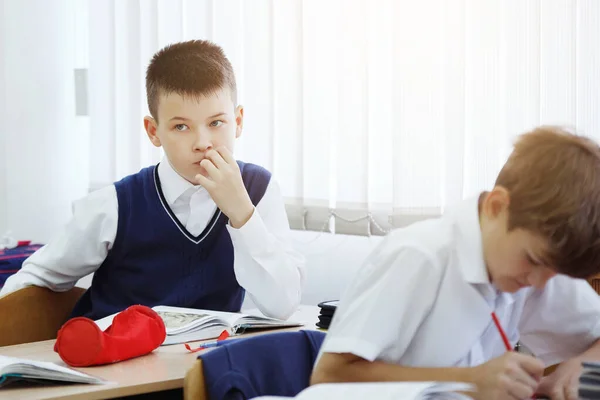 Ein junger Schüler sitzt an einem Schreibtisch in einer Schulklasse. — Stockfoto