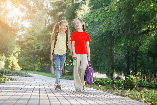 Två tonårsflickor går längs trottoaren i parken. — Stockfoto