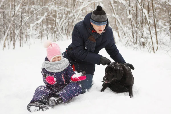Mężczyzna i dziewczyna zabawa z jego czarny labrador retriever w zimie dla — Zdjęcie stockowe