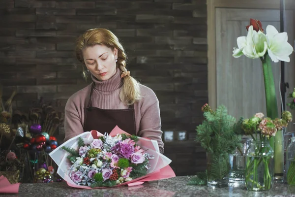 Jolie femme fleuriste d'âge moyen dans un tablier recueille un bouquet . — Photo