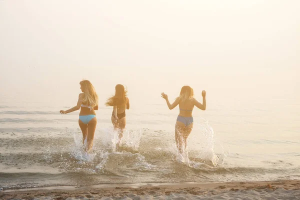 Trzy piękne młode kobiety biegnące do morza. — Zdjęcie stockowe