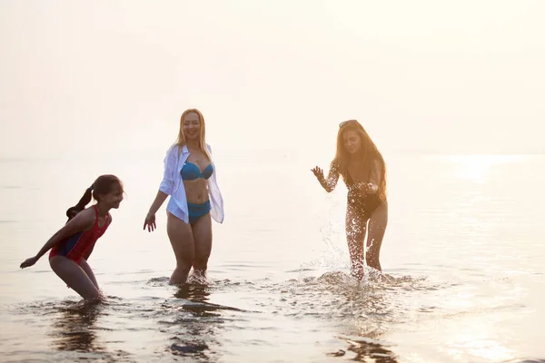 Trzy dziewczyny bawią się w morzu o zachodzie słońca. — Zdjęcie stockowe