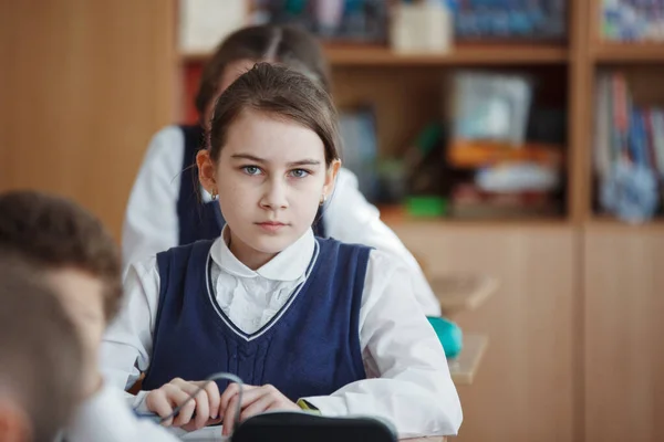 Süße Schulmädchen sitzt an ihrem Schreibtisch in einer Schulklasse. — Stockfoto