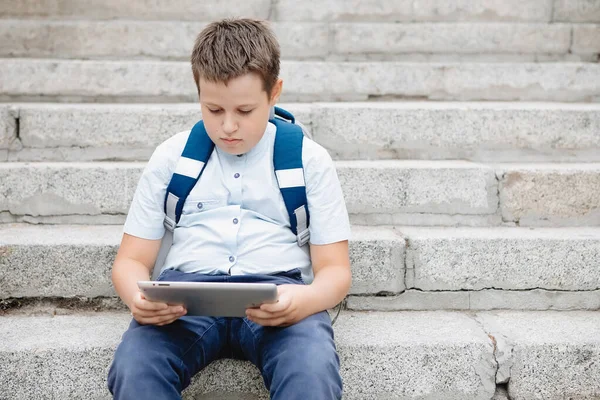 Regordeta adolescente con una tableta y una mochila se sienta en los pasos . —  Fotos de Stock