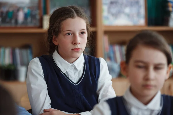 Schattig schoolmeisje zit op haar Bureau in een schoolklas. — Stockfoto