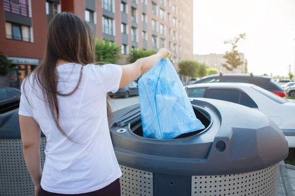 A woman throws a garbage bag in the trash on a city street — Stock Photo, Image