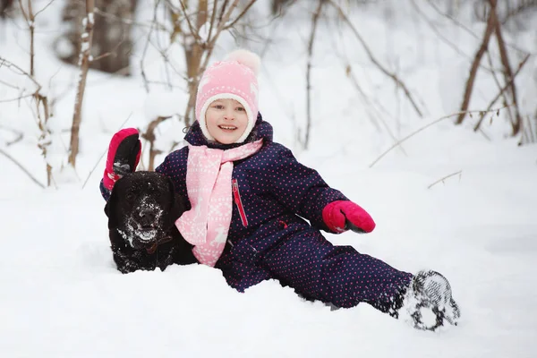 Młoda dziewczyna w śniegu z czarnym labradorem. — Zdjęcie stockowe