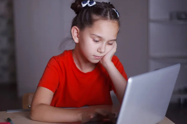 Une jeune fille en T-shirt orange étudie assise à un bureau . — Photo