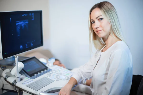 Blonďatá doktorka poblíž ultrazvukového monitoru se dívá na — Stock fotografie