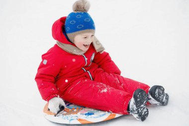 Çocuk karda yuvarlanıyor. Kış Rus eğlencesi. Parlak kırmızı giysi.