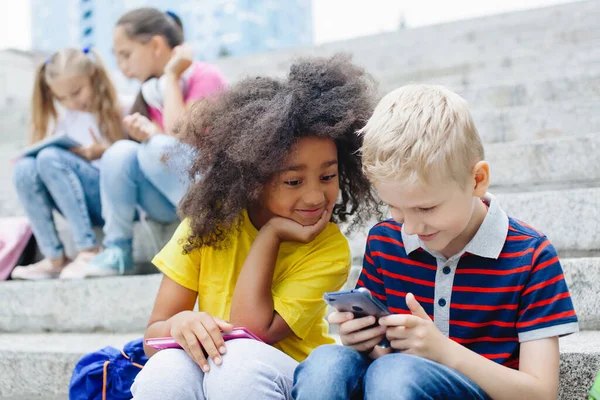 Dos Escolares Una Niña Afroamericana Chico Rubio Están Mirando Smartphone —  Fotos de Stock