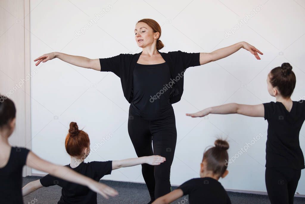 Female trainer shows dance movement with widely spread arms in ballet classes. Selected Focus. Black leotard, hair in a bun, white socks.